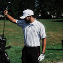 Man on a golf course holding a golf club with trees in the background